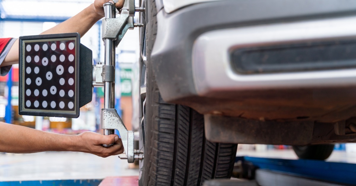 A technician adjusts a wheel alignment sensor on a car tire while the vehicle rests on a service lift.