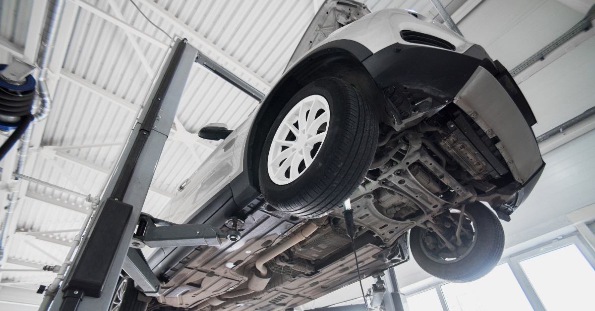 A two-post lift raises a white car above a service bay, exposing the wheels, suspension, and undercarriage.