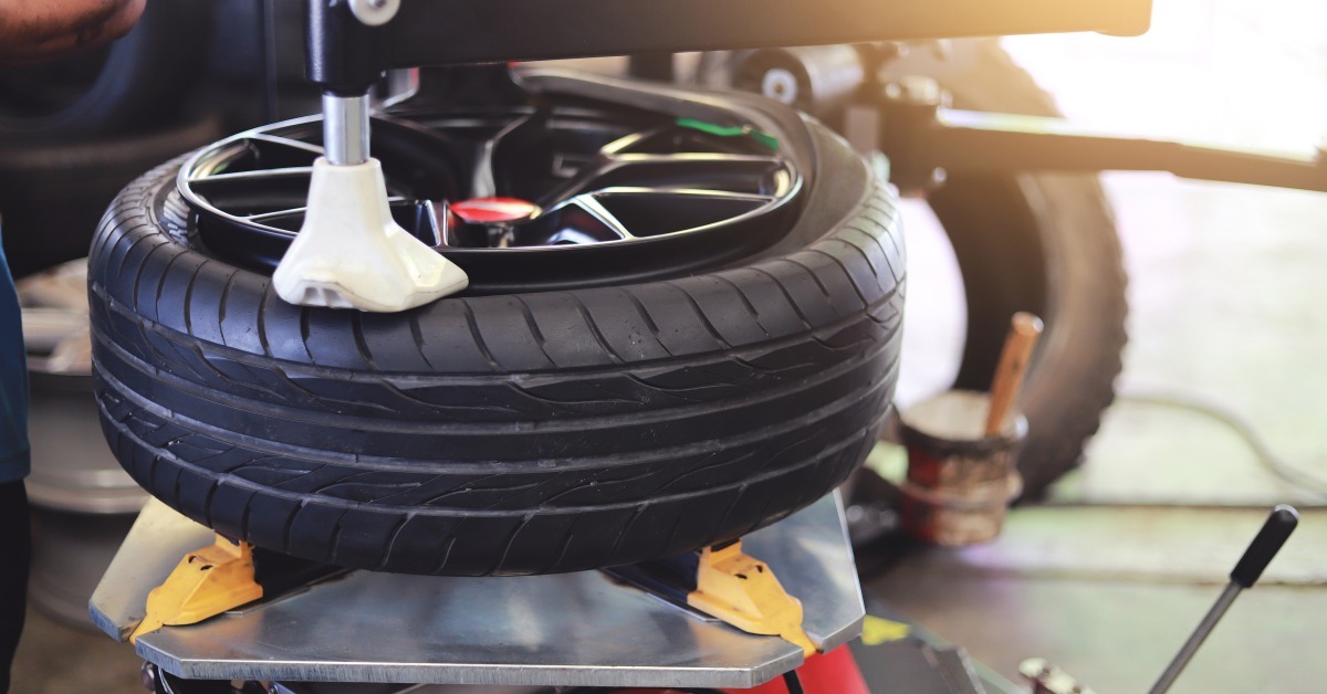 A tire changer holds a black tire with an alloy wheel on its turntable as a mounting head presses against the tire bead.