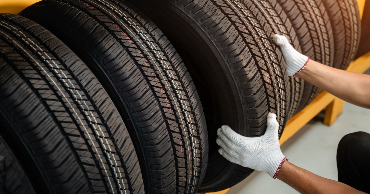 A worker wearing white gloves handles a black tire among several upright tires arranged on a yellow industrial storage rack.